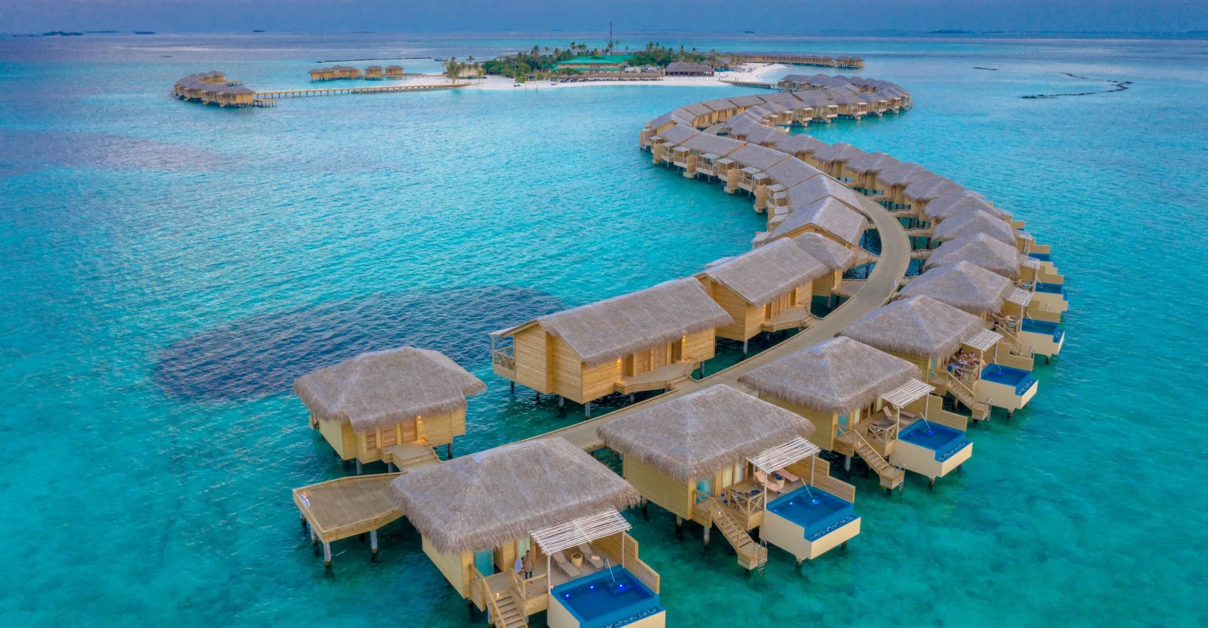Overwater villas with private pools curving across a turquoise lagoon in the Maldives