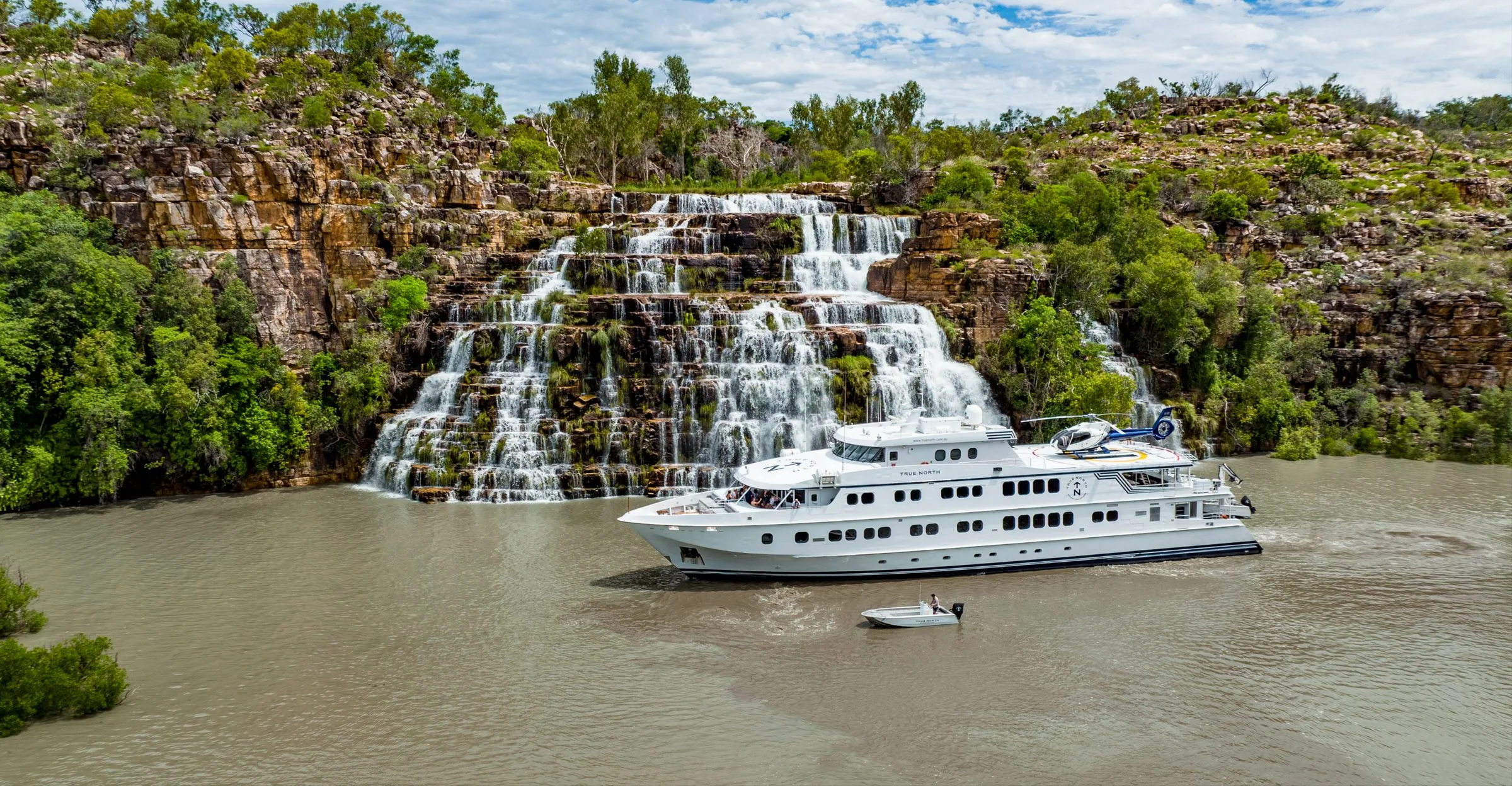 True North at the foot of a tiered waterfall in the Kimberley, with its helicopter on the top deck