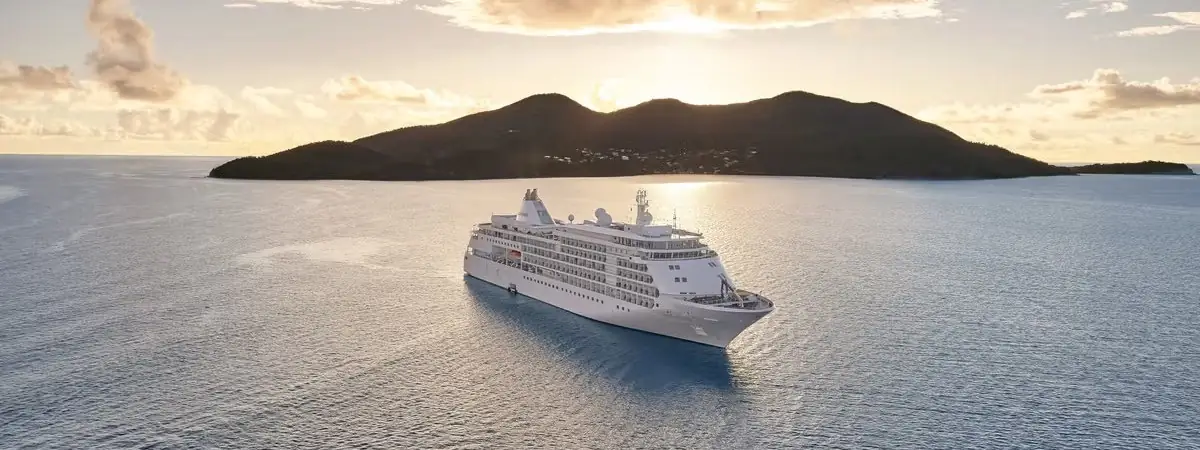 A Silversea ship at anchor off a tropical island at sunset