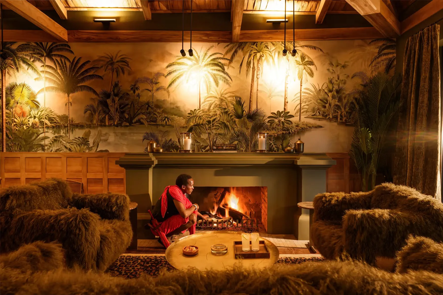 A Maasai host tending the fire in a lodge lounge beneath a palm-tree mural