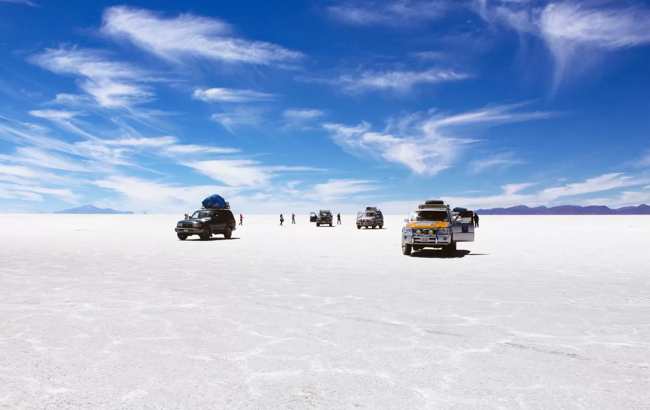 Four-wheel drives crossing the white Salar de Uyuni beneath a blue sky