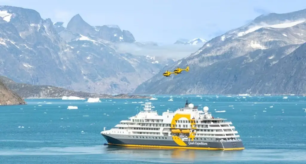 A Quark Expeditions ship with helicopters in a Greenland fjord