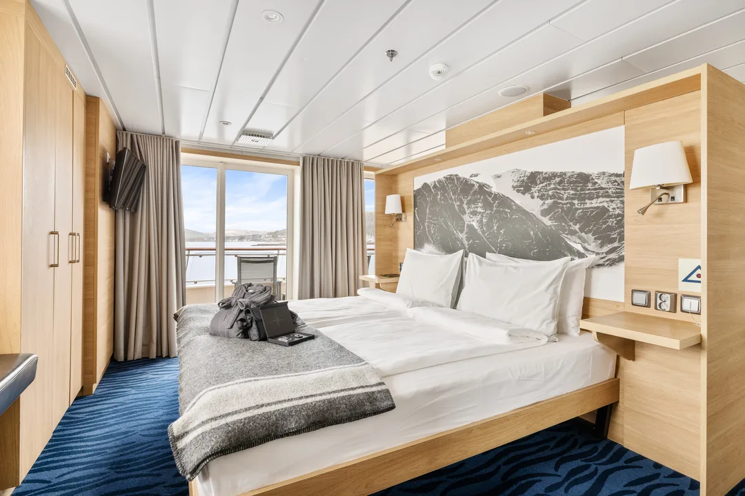A light timber cabin with a double bed and a balcony looking out to the water