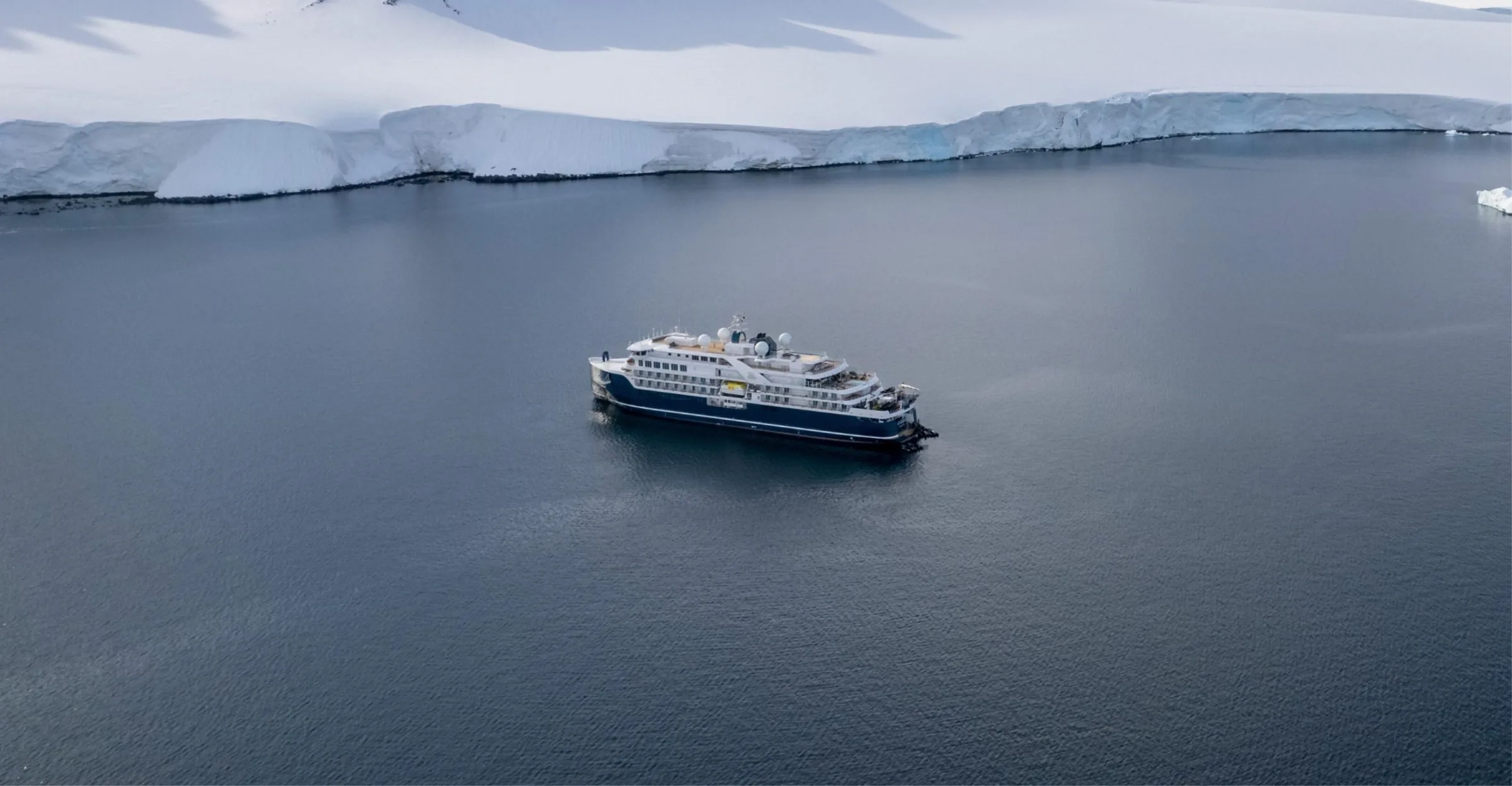 A Swan Hellenic expedition ship in calm water beneath an Antarctic ice shelf