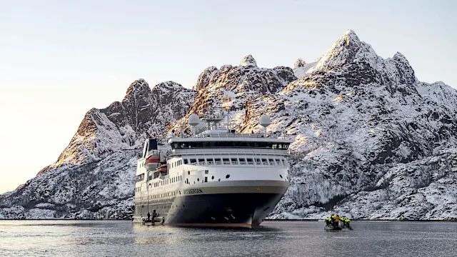 MS Spitsbergen at anchor beneath snow-covered mountains, with a Zodiac alongside