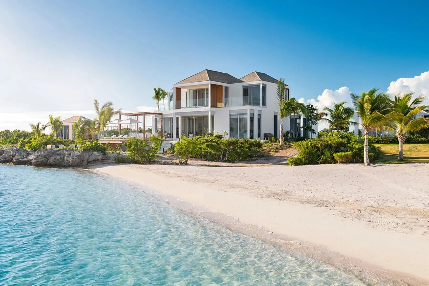 A white two-storey beachfront villa among palm trees, on a quiet beach with clear turquoise water