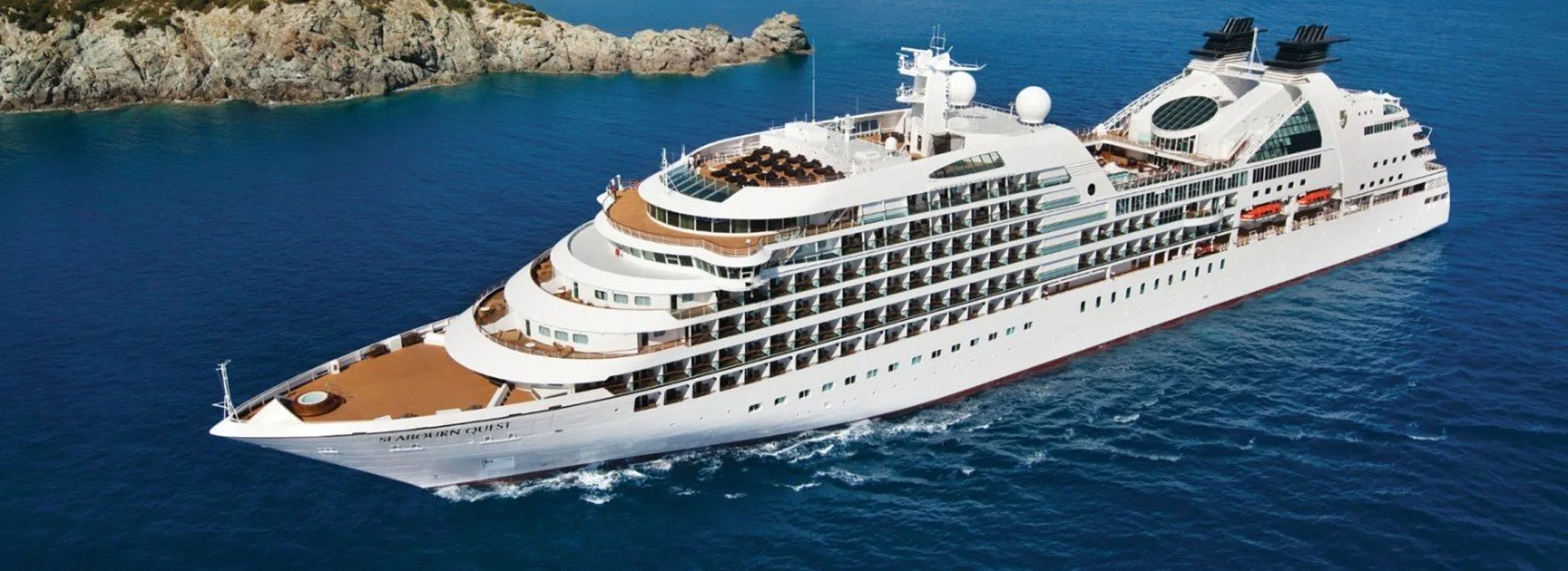 Seabourn Quest at sea off a rocky coastline