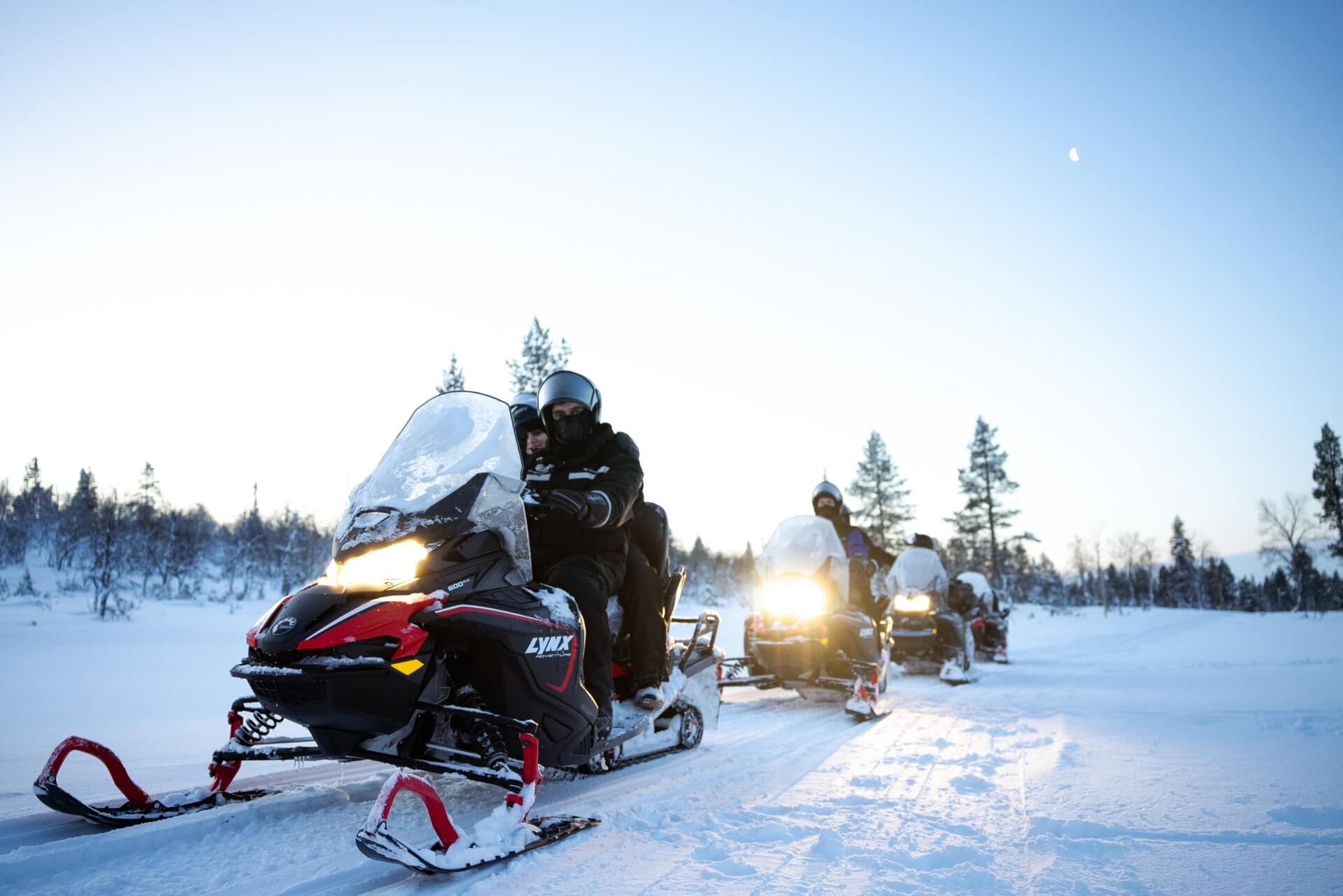 A line of snowmobiles crossing open snow at dusk