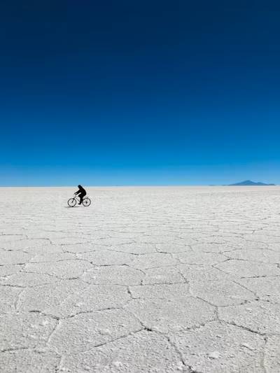 A lone cyclist crossing the cracked white salt beneath a deep blue sky