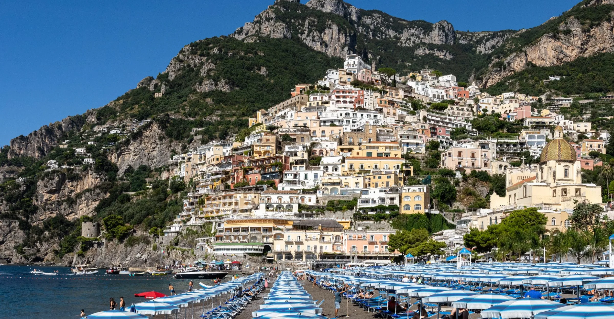Positano's pastel houses rising above striped beach umbrellas on the Amalfi Coast